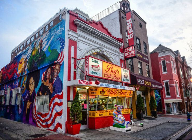 The bright red‑and‑white storefront of Ben’s Chili Bowl features its iconic signage and a large colorful mural along the side of the building.