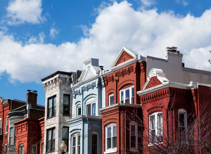 A row of colorful historic townhouses with ornate details stands under a bright blue sky with scattered clouds.
