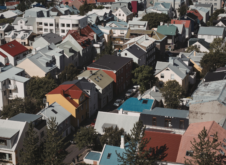 An aerial view shows a dense neighborhood of colorful rooftops and closely packed homes with scattered trees.