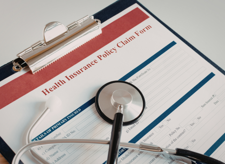 A clipboard holds a health insurance claim form with a stethoscope resting across the top.