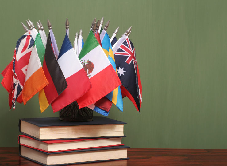A cluster of small international flags stands in a circular holder atop a stack of books against a green background.
