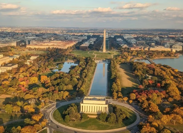 A wide aerial view shows the Lincoln Memorial, Reflecting Pool, and Washington Monument aligned along the National Mall surrounded by autumn trees.