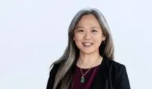 Person with long gray-streaked hair wearing a dark blazer over a burgundy top. 