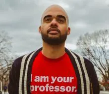A man wearing a bright red T-shirt with bold white text that reads “I am your professor.”
