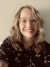 Person with shoulder-length wavy hair wearing a dark collared shirt featuring a light-colored floral pattern.