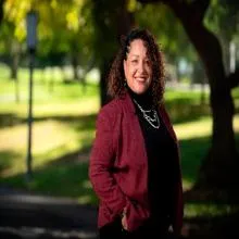 Woman wearing maroon blazer standing with hand in pocket outside.