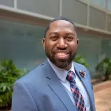 Man wearing tie and blazer smiling at the camera.