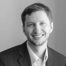  Black-and-white headshot of an adult wearing a dark blazer and light collared shirt, against a plain background.