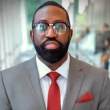 Man with glasses, gray suite and red tie looking straight to camera.