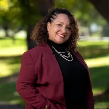 Woman wearing maroon blazer standing with hand in pocket outside.
