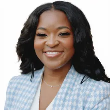 A women smiling toward the camera wearing a blue and white checker blazer and white blouse.
