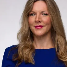 Head-and-shoulders professional portrait of a person with long hair against a light gray background.